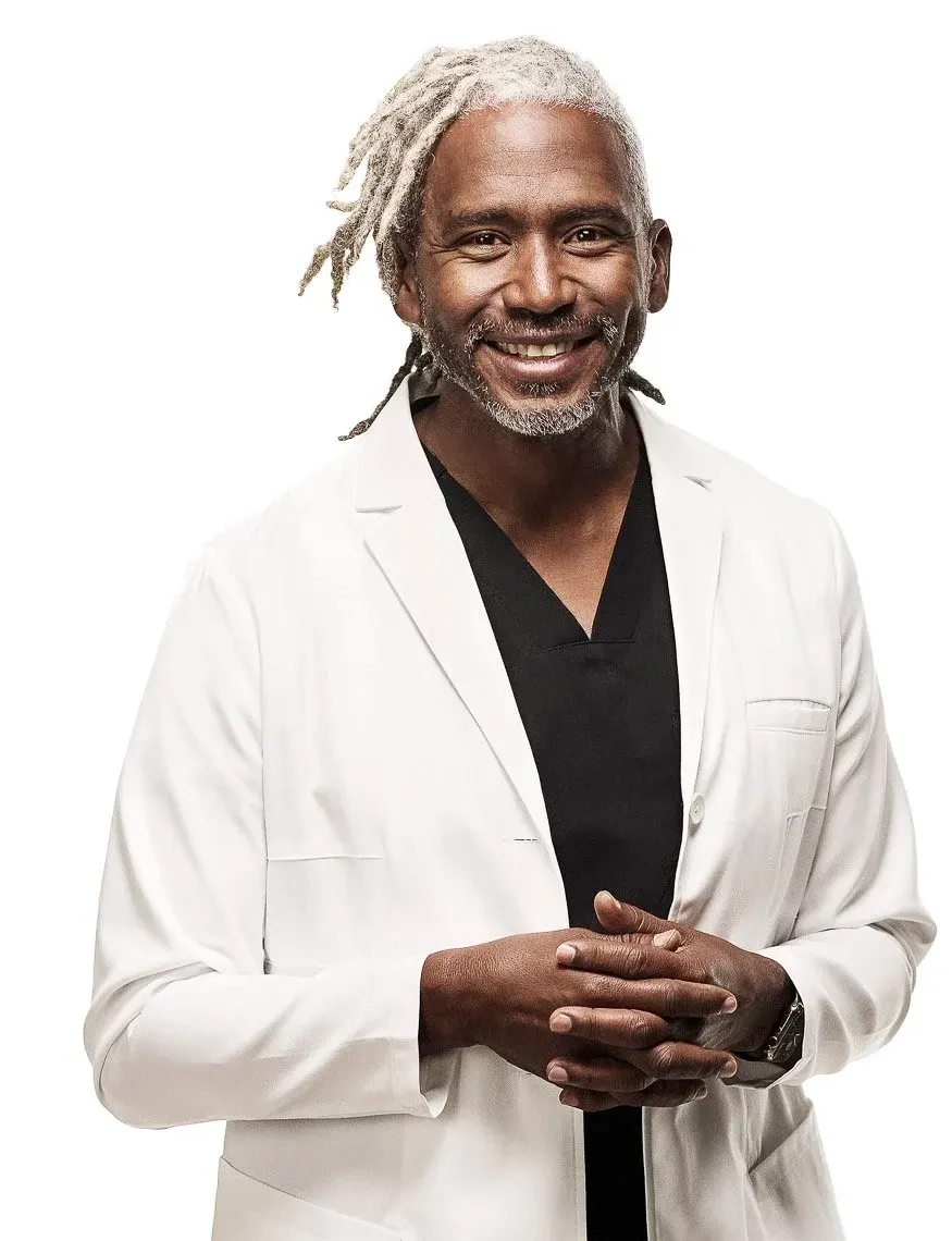 A middle-aged man with gray dreadlocks in a white jacket, smiling